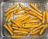En hög med gyllene, krispiga pommes frites ligger på ett galler i en plåt. Perfekt för en snabb fika!