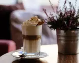 Ein hoher Frappe Espresso mit Sahne, Zimt und einem Keks. Daneben eine Topfpflanze.