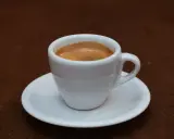 Ein kleiner weißer Becher mit cremigem, doppeltem Espresso, italienisch zubereitet, steht auf einer Untertasse.