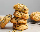 Stapel von leckeren, hausgemachten veganen Keksen mit Schokoladenstückchen und Pistazien. Ein Keks liegt daneben, ein weiterer auf einem Gitter.