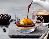 Heißer Espresso fließt über eine Kugel Vanilleeis in einem Glas. Ein köstlicher Affogato al caffè, bereit zum Genießen.