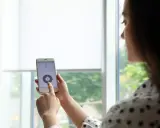 Kobieta steruje roletami z telefonu, dotykając ekranu smartfona.