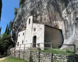 Piccolo eremo di San Valentino incastonato nella roccia, con un campanile a vela e un sentiero che conduce al suo ingresso.