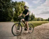 Mężczyzna w kasku i okularach jedzie na rowerze typu cross po ścieżce w parku.