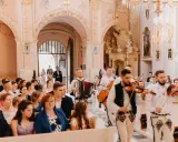 Muzycy w strojach ludowych grają tradycyjne pieśni na ślub w kościele. W tle para młoda wchodzi do świątyni.