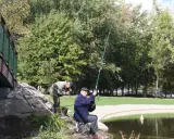 Dwóch wędkarzy łowi ryby nad jeziorem w Chojnicach. Jeden z nich właśnie wyciąga zdobycz.