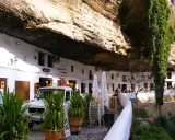 Häuser unter Felsvorsprung in Setenil de las Bodegas. Ein Auto und Pflanzen vor dem "El Gastor" Bar.