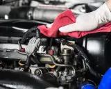 Mano enguantada realiza limpieza de piezas mecánicas de motor con paño rojo.