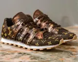 Brązowe buty sportowe Louis Vuitton z monogramem na marmurowym tle.