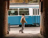 Una ragazza cammina in un vicolo, un tram blu sfreccia sullo sfondo. Una foto vedo non vedo che cattura un momento fugace.