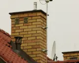 Dwa kratkowane otwory wentylacyjne na ceglanym kominie, zapewniające prawidłowe odpowietrzenie pionu sanitarnego zgodnie z normą.