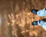 Pintura para corcho con un diseño de baldosas y sombras de luz. Se ven unos pies con zapatos oscuros y pantalones vaqueros.