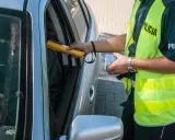 Policjant bada kierowcę alkomatem, sprawdzając, czy nie ma **alkoholu w organizmie**. Kierowca siedzi za kierownicą, a funkcjonariusz trzyma urządzenie przy jego twarzy.
