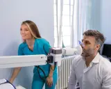 Mann macht Lungenfunktionstest, Arztin überwacht. Ergebnisse zeigen 70 Prozent Lungenfunktion.