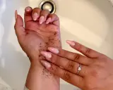 Manos con uñas largas y rosadas, cubiertas de gránulos oscuros. Parece un autobronceador mal aplicado que se está intentando lavar.