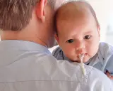 Un padre tiene in braccio il suo neonato, che ha un rigurgito visibile.
