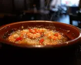 Gambas al ajillo burbujeantes en cazuela de barro, con guindillas rojas y vapor ascendiendo.