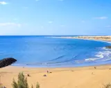 Sonniger Strand auf Gran Canaria mit goldenem Sand, türkisfarbenem Meer und einigen Menschen, die die Sonne genießen.