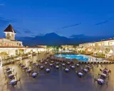 Wieczorny widok na kompleks hotelowy Gural Premier Tekirova z basenem i oświetlonymi budynkami, w tle góry.