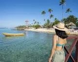 Kobieta w kapeluszu podziwia plażę z latarnią i palmami. Czy to Puerto Plata czy Punta Cana?