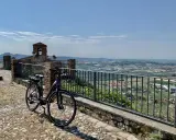 Bicicletta pronta per esplorare il **percorso fiume Marecchia**, con vista panoramica sulla valle e un antico campanile.