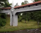 Mostek z wieżyczką, jedna z atrakcji Lądka Zdroju, przerzucony nad strumieniem, otoczony zielenią.