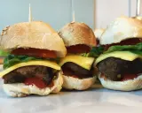 Drei leckere Slider Burger mit Käse, Tomate und Salat auf einem Teller.