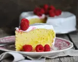 Wilgotne ciasto tres leches z malinami na talerzyku, w tle cały tort.