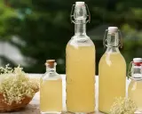 Syrop z kwiatu czarnego bzu przepis. Wesołe butelki z domowym syropem i koszyk pełen kwiatów czarnego bzu.