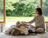 Donna medita su come iniziare il decluttering, circondata da vestiti e scatole vuote.