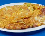 Złocisty omlet z warzywami i kawałkami kiełbasy, idealny przykład, jak się robi omlet dietetyczny.
