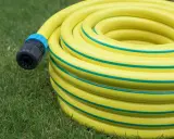 Un tuyau d'arrosage jaune enroulé sur l'herbe, avec un connecteur noir et bleu. Le diamètre du tuyau d'arrosage est visible dans son enroulement.