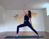 Kvinna i krigarställning i ett ljust rum med solrosmålning på väggen. En lugn yoga andrum.