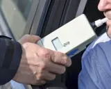 Policjant bada kierowcę alkomatem. Za jazdę po alkoholu, nawet 1 promil, zabierają prawo jazdy.