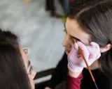 Stylistka w różowej rękawiczce aplikuje hennę pudrową na brwi klientki. Efekt naturalny, jak po hennie zwykłej, ale trwalszy.
