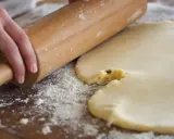 Mains roulant une pâte à biscuits trop sableux. Farine saupoudrée sur la planche en bois.