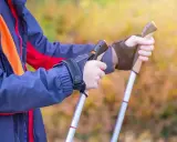 Osoba w kurtce ćwiczy, jak chodzić z kijkami trekkingowymi. Dłonie pewnie trzymają uchwyty, gotowe do marszu.