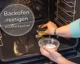 Backofen reinigen mit Backpulver: Eine Hand schrubbt mit einem Schwamm, die andere hält eine Schüssel mit der Reinigungspaste.