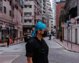 Uomo con bandana blu e mascherina nera in una foto di strada con edifici alti e traffico.