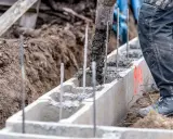 Betoniarka wylewa beton do szalunku. Pracownik w spodniach roboczych stoi obok. To kluczowy etap, by wiedzieć, jak obliczyć ilość betonu.