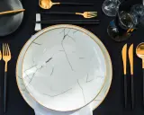 Un ensemble élégant pour les arts de la table : assiettes marbrées, couverts dorés et noirs, verres sombres.
