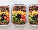 Drei Glasbehälter mit einem gesunden Essensplan für Fitness: Linsen, Gurken, Oliven, Tomaten, Mais und brauner Reis.
