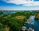En vacker promenad i Stockholm med grönskande träd, en bro över vattnet och många segelbåtar i hamnen.