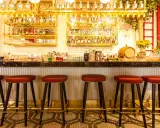 Bar con botellas doradas y taburetes rojos. Ideas para decorar un bar con poco dinero: ¡la iluminación y los detalles marcan la diferencia!