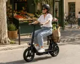 Une femme souriante fait une course de trottinette électrique, son panier rempli de courses.