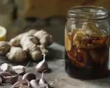 Słoik z imbirem i miodem, obok czosnek i cytryna – naturalny antybiotyk na gardło gotowy do użycia.