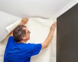 Hombre colocando papel tapiz texturizado, un paso para insonorizar habitación y mejorar la acústica.