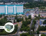 Widok z lotu ptaka na kompleks budynków, w tym duży, jasny budynek z niebieskimi akcentami, przypominający umed w Łodzi. Widać parkingi, drogi i zieleń.