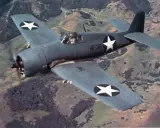 F6F Hellcat fliegt über hügelige Landschaft.