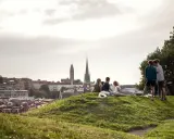 Vänner njuter av utsikten över Haga, Göteborg. En grupp unga människor sitter på en gräskulle med staden i bakgrunden.